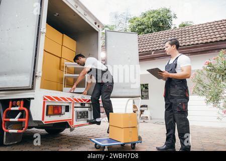 Uniformierte Mitarbeiter der Umzugsfirma entladen Kisten und Möbel aus dem Lkw, die sich hervorragend auszeichnen Stockfoto
