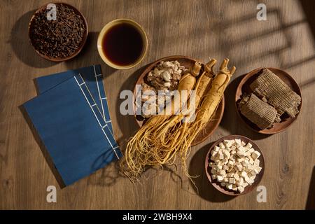 Aromatischer Ingwer, Szechuan Lovage Rhizome und Ginseng-Wurzeln auf einem runden Gericht. Zwei Bücher, eine Schüssel mit Tonic und anderen Medikamenten arrangierten aro Stockfoto