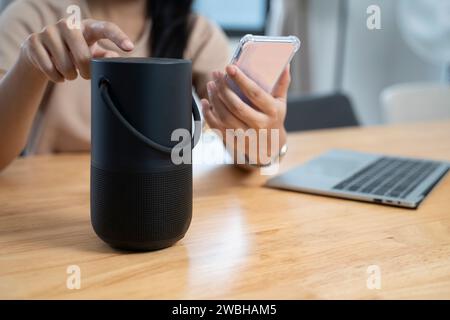 Junge Frau, die intelligente Lautsprechergeräte in ihrem Zuhause durch die Verwendung von Smartphones bedient. Stockfoto