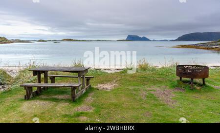 Sitzbereich am Strand von Sommarøya, Grillbereich am Ufer des Nordatlantiks, in Troms, Norwegen. Parkbank aus Holz mit Tisch, Esstisch, Kamin Stockfoto