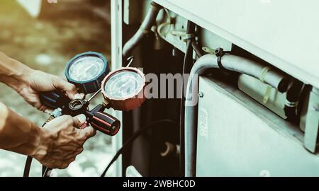 Luftreparaturmechaniker mit Messgeräten zum Befüllen von industriellen Klimaanlagen und zur Überprüfung der Wartung der Außenluftkompressoreinheit. Stockfoto