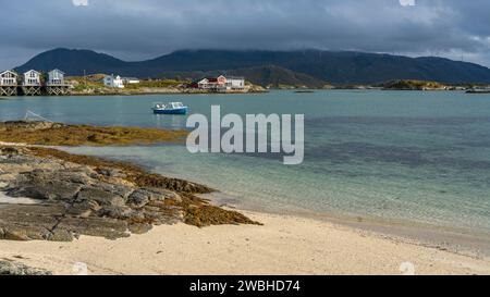 Weißes Ruderboot am weißen Sandstrand von Sommarøy in Troms, Norwegen. Yacht im Hintergrund das türkisfarbene Wasser des Atlantiks mit Inseln Stockfoto