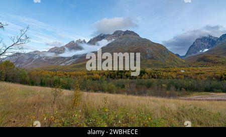 Steile Berge in den Lyngenalpen von Troms in Norwegen. Tiefe Gletschertäler mit herbstbunten Bäumen und felsigen Gipfeln im Herbst. Wundervolle, ruhige Natur Stockfoto