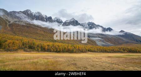 Steile Berge in den Lyngenalpen von Troms in Norwegen. Tiefe Gletschertäler mit herbstbunten Bäumen und felsigen Gipfeln im Herbst. Wundervolle, ruhige Natur Stockfoto