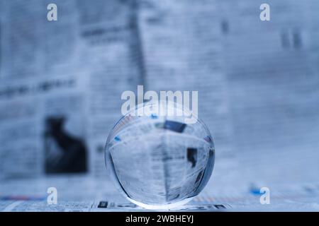 Eine Glaskugel zeigt die Buchstaben im Inneren, mit einer Zeitung im Hintergrund. Stockfoto