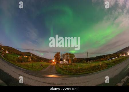 Wunderschöne grüne Nordlichter über einem Fjord und einem Haus auf der Insel Kvaloya in der Nähe von Tromsø. Tanzende Polarlichter über einem Berg, aurora borealis Stockfoto