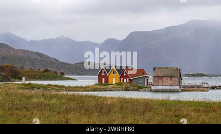 rote und gelbe Häuser am Strand des Atlantik auf der Insel Hillesøya bei Sommarøy, Troms, Norwegen. Landschaft Kalenderfoto mit Bergen im Hintergrund Stockfoto