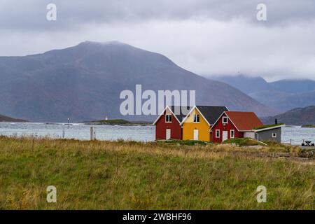 rote und gelbe Häuser am Strand des Atlantik auf der Insel Hillesøya bei Sommarøy, Troms, Norwegen. Landschaft Kalenderfoto mit Bergen im Hintergrund Stockfoto