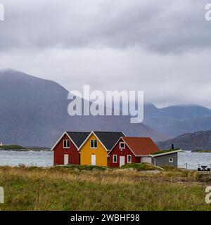 rote und gelbe Häuser am Strand des Atlantik auf der Insel Hillesøya bei Sommarøy, Troms, Norwegen. Landschaft Kalenderfoto mit Bergen im Hintergrund Stockfoto