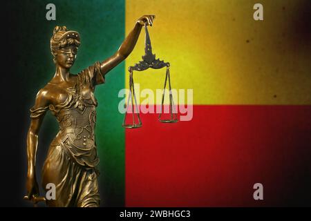 Nahaufnahme einer kleinen Bronzestatuette von Lady Justice vor einer Benin-Flagge. Stockfoto