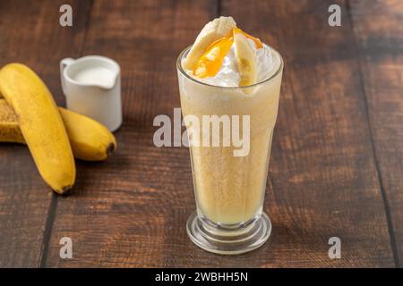 Bananen-Smoothie in Glasbecher auf Holztisch Stockfoto