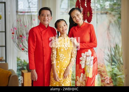 Lächelnde Eltern und ihre Teenager-Tochter tragen traditionelle Kostüme, wenn sie zu Hause Tet feiern Stockfoto