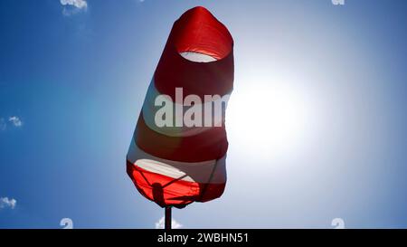 Windsocke vor blauem Himmel. Anzeige mit Wind vor der Hintergrundbeleuchtung der Sonne. Pistensicherheits- und Messwerkzeug, Windsocke verwendet. Stockfoto