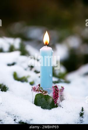 Handgefertigter Weihnachtskerzenhalter aus Eis, rosa calluna Blütenzweige mit brennender blauer Kerze im schneebedeckten Garen. Winterdekoration im Freien Stockfoto
