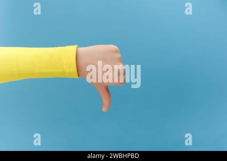 Nahaufnahme der Frauenhand mit dem Daumen nach unten, posiert isoliert über blauer Hintergrundwand im Studio mit Kopierraum für Werbeinhalte oder des Stockfoto