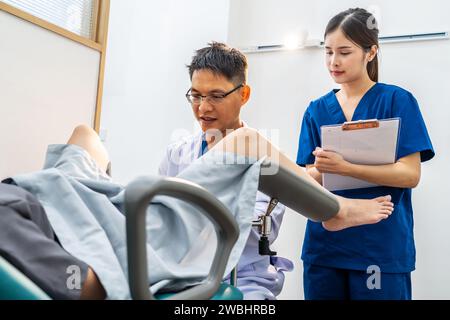 Männlicher asiatischer Arzt, der interne Untersuchungen an weiblicher Patientin im Krankenhauszimmer durchführt. Sie diskutieren über Krankheit mit weiblichen Patienten im Krankenhaus Stockfoto