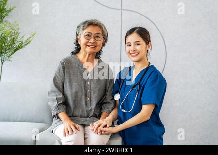 Junge asiatische Ärztin oder Krankenschwester unterstützt ältere Patienten gerne. Doktor und Seniorengroßmutter sitzen lächelnd und schauen zusammen in die Kamera Stockfoto