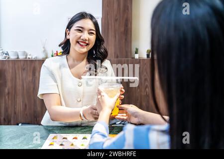 Der Kellner servierte einem Gast, der eine asiatische Frau am Tresen im Restaurant war, ein Glas frischen Saft, die Angestellten der Saftbar servierten dem Gast Getränke Stockfoto