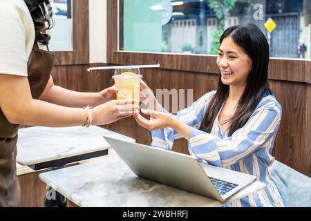 Der Kellner servierte einem Gast, der eine junge asiatische Frau auf dem Tisch im Restaurant war, ein Glas frischen Saft, die Angestellten der Saftbar servierten dem Gast Getränke Stockfoto