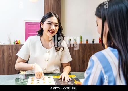 Junge asiatische schöne weibliche Kundin wählen Kaffee oder Saft Artikel. Mit einer jungen Barista, die am Café- oder Restauranttheke arbeitet, Stockfoto
