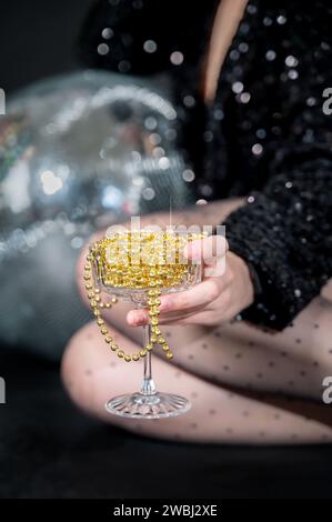 Sektglas voller goldener Weihnachtsperlen als alkoholfreies Getränk in der Person mit Discokugel auf dem Hintergrund Stockfoto