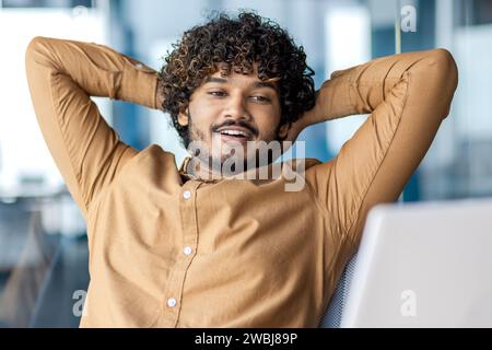 Gut gelungener Geschäftsmann hat Arbeit und Projekt im Büro am Arbeitsplatz erfolgreich abgeschlossen, Mann mit Händen hinter dem Kopf, der auf den Laptop blickt, zufrieden mit den Ergebnissen. Stockfoto