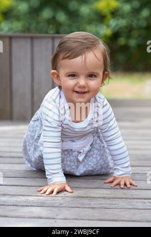 Baby Mädchen, krabbeln draußen und Porträt auf dem Boden, Entwicklung und Wachstum von Kindern mit sensorischer Koordination. Mädchen, Kognition und gesund in guter Laune Stockfoto