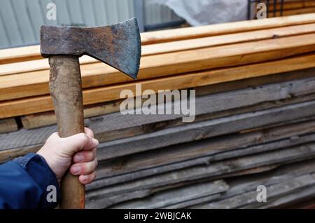 Mann mit Axt. Axt in der Hand. Ein starker Mann hält eine Axt in den Händen vor dem Hintergrund von Feuerholz. Selektiver Fokus, unscharfer Hintergrund Stockfoto