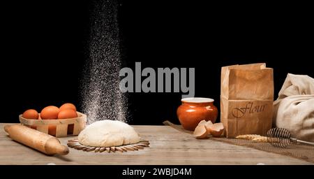 Brot kochen. Der Teig liegt auf einem hölzernen Küchentisch und bestreut mit Mehl. Auf dem Küchenbrett sind Eier in einem Korb, eine Tüte Mehl, A Stockfoto