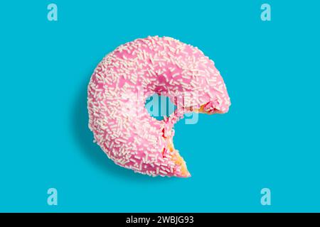 Ein gebissener rosafarbener Donut mit weißen Streuseln auf blauem Hintergrund. Frischer Donut mit rosafarbener Glasur. Stockfoto