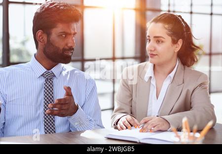 Junge indische Mentorentrainerin, die mit einer Kollegin spricht, die eine Trainee unterrichtet, und mit einer Arbeitskollegin ein Geschäftsgespräch führt Stockfoto