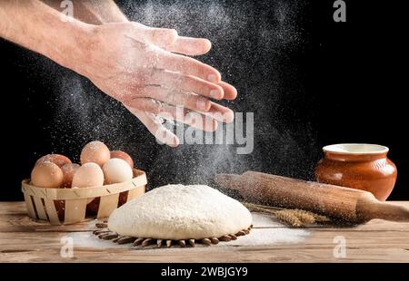 Der Bäcker klatscht sich mit Mehl über den Teig. Ein Mann bereitet hausgemachtes Brot in der Küche zu. Gesunde Ernährung. Stockfoto