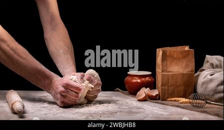 Ein Bäcker kocht Brot in der Küche. Ein Mann knetscht Teig mit den Händen auf einer hölzernen Küchenarbeitsfläche. Hausmannskonzept Stockfoto