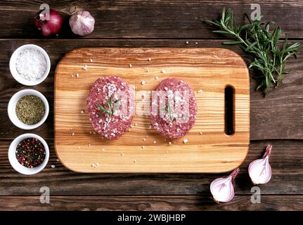 Rohe Fleisch runde Schnitzel - zum Kochen hausgemachter Hamburger. Schnitzel auf einem hölzernen Schneidebrett. Flache Lagen. Draufsicht. Arbeitsplatte aus Holz. Stockfoto