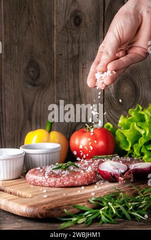 Rohe Bio-Fleischkoteletts. Kochen Sie Salz auf Fleischkoteletts auf einem hölzernen Schneidebrett. Zubereitung von Fleisch für einen köstlichen hausgemachten Hamburger. Stockfoto