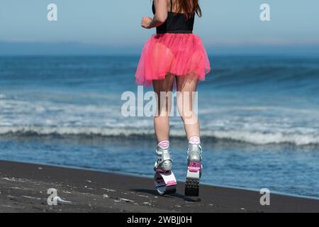 Rückansicht der Beine der Sportlerin in Kangoo springt Sportschuhe, kurzer rosa Rock und Badeanzug, die draußen am Strand laufen Stockfoto