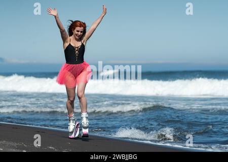 Glückliche Sportlerin in Kangoo springt Stiefel, schwarzen Badeanzug und kurzen Rock, der auf schwarzem Sand springt und läuft Stockfoto