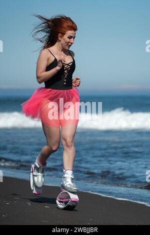 Sportsportlerin Kangoo springt Stiefel, schwarzer einteiliger Badeanzug und kurzer rosafarbener Rock beim Laufen und Springen Stockfoto