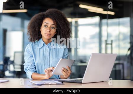 Porträt einer seriösen, selbstbewussten Programmiererin im Büro am Arbeitsplatz, Geschäftsfrau, die konzentriert und nachdenklich auf die Kamera blickt, einen Tablet-Computer hält, neue Software testet. Stockfoto