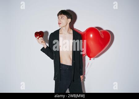 Mann in schwarzem Hemd mit rotem Herzballon und Geschenk auf grauem Hintergrund, Valentinstag Stockfoto