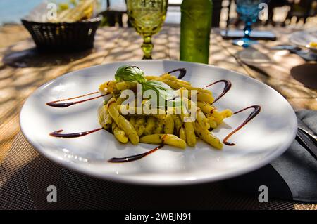 Penne Pasta auf einem weißen Teller auf Sardinien, mit Pesto, Balsamico-Essig und frischen Basilikumblättern. Stockfoto