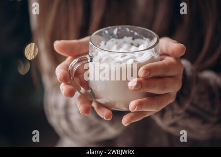 Transparenter Glasbecher Kakao mit Marshmallows in weiblichen Händen. Nahaufnahme. Silvester-Weihnachtsportrait. Stockfoto