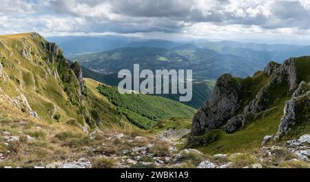 Blick auf die Berge von Vlasic bei Travnik, felsige Hänge, die im Sonnenlicht mit Gras bewachsen sind, und trübe Berge in der Ferne während des bewölkten Tages Stockfoto