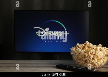 Nikolaev, Ukraine - 20. November 2021. Ein Mann hält eine Disney-Fernbedienung mit einem neuen Bildschirm auf einem Popcorn-Fernseher. Disney ist ein Online-Video-Streaming-Abonnement Stockfoto