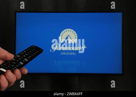 Nikolaev, Ukraine - 20. November 2021. Mann mit Fernbedienung in der Hand und Paramount Pictures Corporation Logo im Hintergrund. Draufsicht. Stockfoto