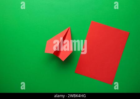 Flache Lage aus rotem Papier und leerem Papier auf grünem Hintergrund. Draufsicht Stockfoto