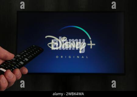 Nikolaev, Ukraine - 20. November 2021. Iman mit TV-Fernbedienung in der Hand und Disney Logo Hintergrund. Draufsicht. Stockfoto