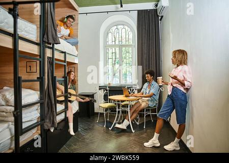 Glückliche multiethnische Freunde, die Spaß haben und sich in einem gemütlichen Zimmer der Jugendherberge, Studentenleben ausruhen Stockfoto