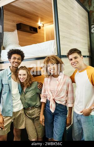 Fröhliche und trendige multikulturelle Freunde lächeln in der Kamera im Zimmer der modernen Herberge, Reisende Stockfoto