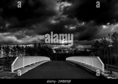 Landstraße, die über eine Brücke führt, Eisengeländer, Himmel voller Regenwolken, schwarz-weiß Stockfoto